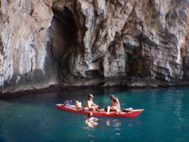 three people sititng on a kayak one person in the water surrounded by high cliffs in montenegro 